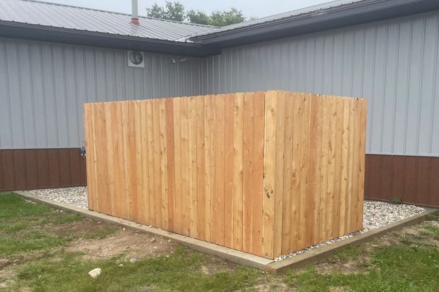 Wooden privacy fence enclosure beside a gray building on a grassy yard.