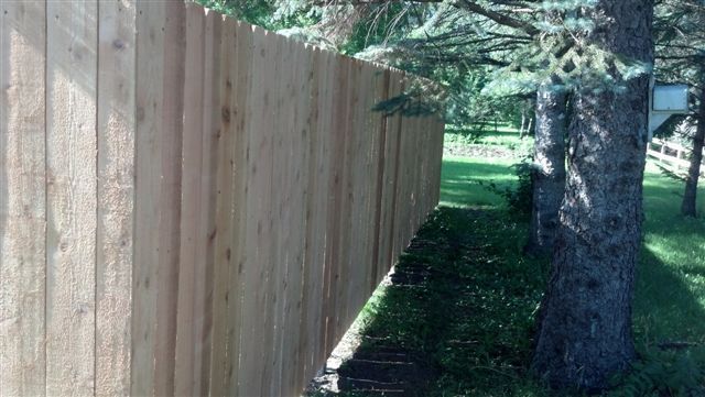 Wooden fence along a shaded path beside a tree in a grassy yard