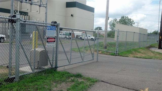 Chain-link gate at an industrial facility beside a paved driveway and grassy area