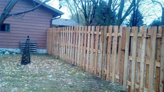 Wooden backyard fence beside a pink house in a leaf-covered yard on a cloudy day