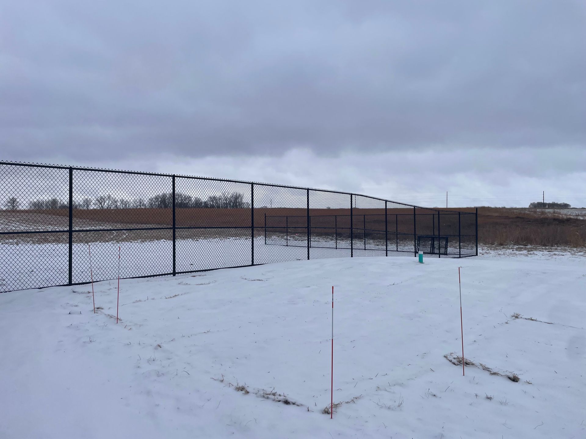 Snow-covered field beside a chain-link fence under a cloudy sky.