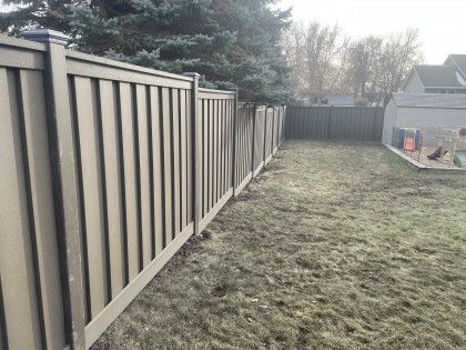 Narrow grassy yard beside a gray wooden privacy fence with evergreen trees in the background