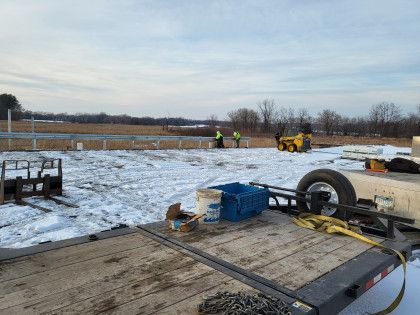 Snowy construction site with workers in neon vests, a yellow machine, and trailers in the foreground