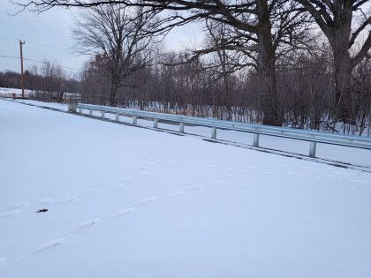 Snow-covered roadside with a guardrail and bare trees in a winter landscape