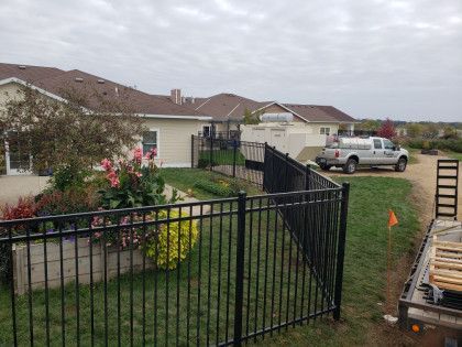 Backyard with black metal fence, flowers, house, and parked pickup truck under cloudy sky