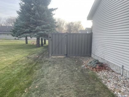 Backyard beside a house with a wooden fence gate, grass, and a pine tree in the yard
