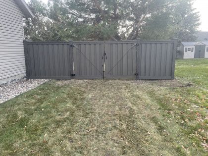 Gray vinyl fence and gate beside a house, with a grassy yard and trees in the background.