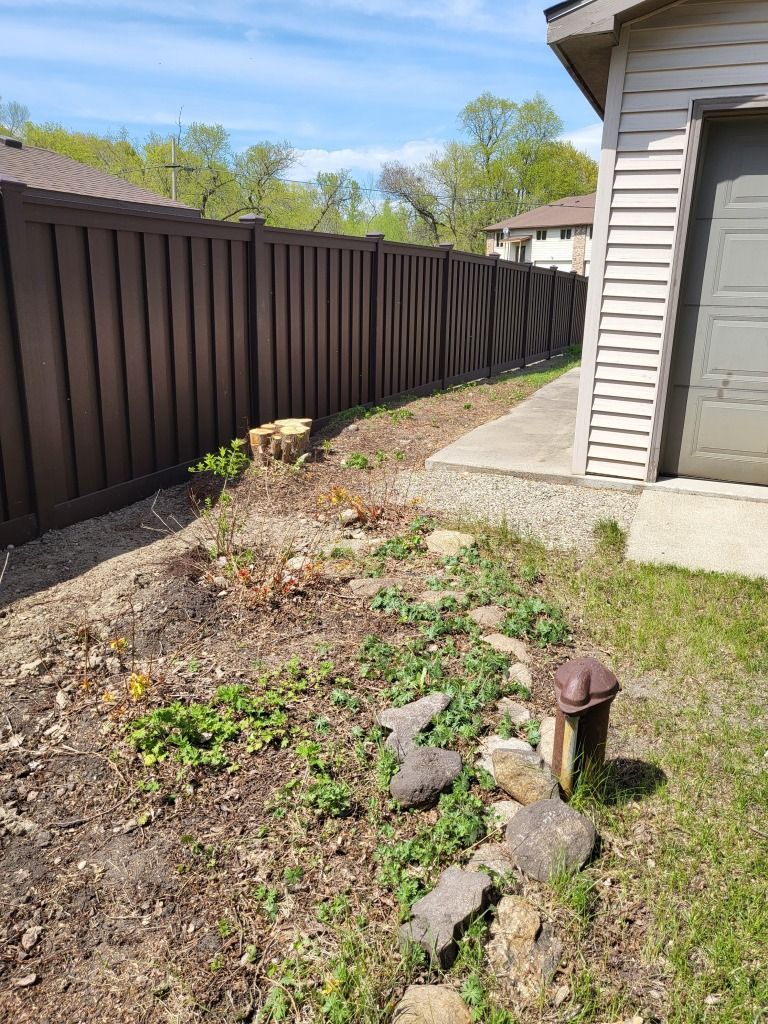 Backyard side yard with dark fence, house siding, and a small garden bed with rocks and a rusty pipe.