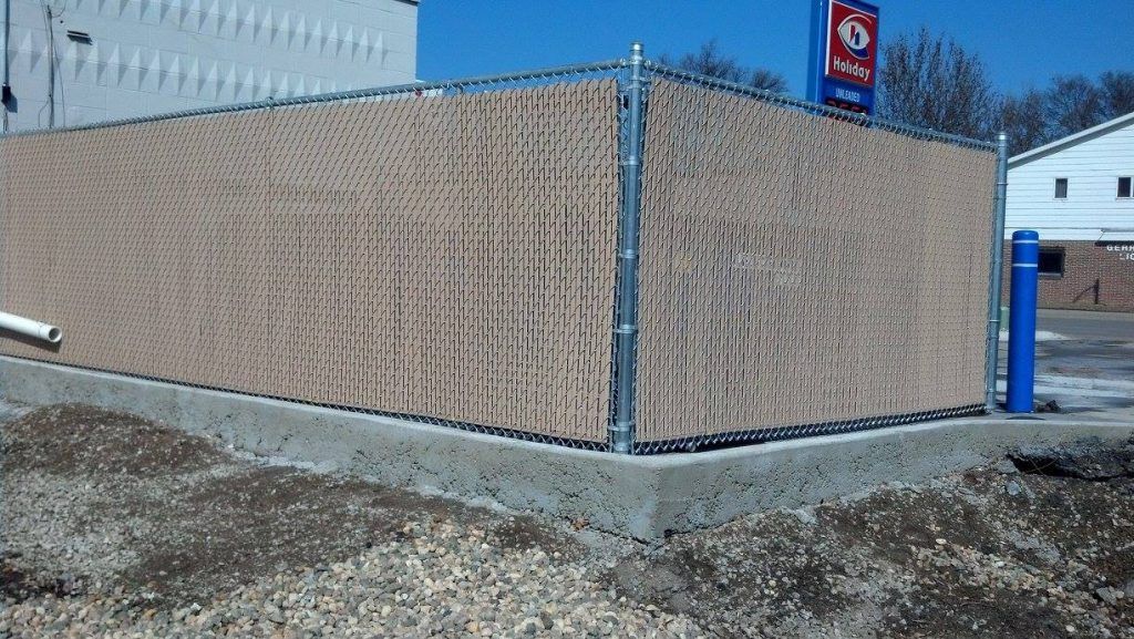 Industrial building corner with tan fencing, gravel ground, and a blue utility pole near a white wall.