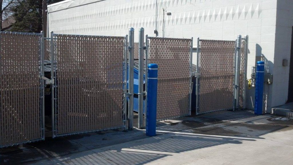 Blue parking gate beside chain-link fence in an industrial lot, with a white wall and shadows.