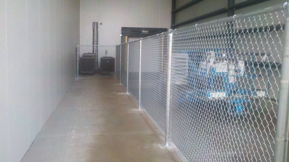 Narrow indoor storage aisle with chain-link fence on the right and white wall on the left.