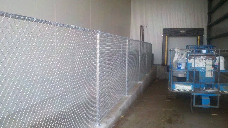 Chain-link fence inside an industrial warehouse, with a blue utility vehicle parked on the right.