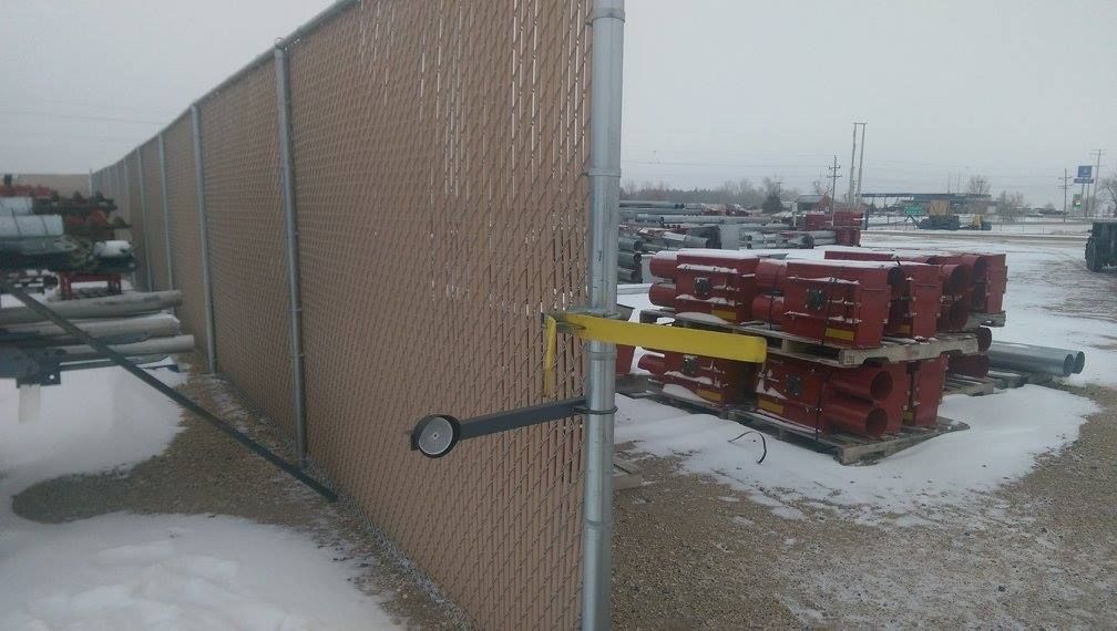 Snowy industrial yard with stacked red pallets beside a chain-link fence and warehouse wall