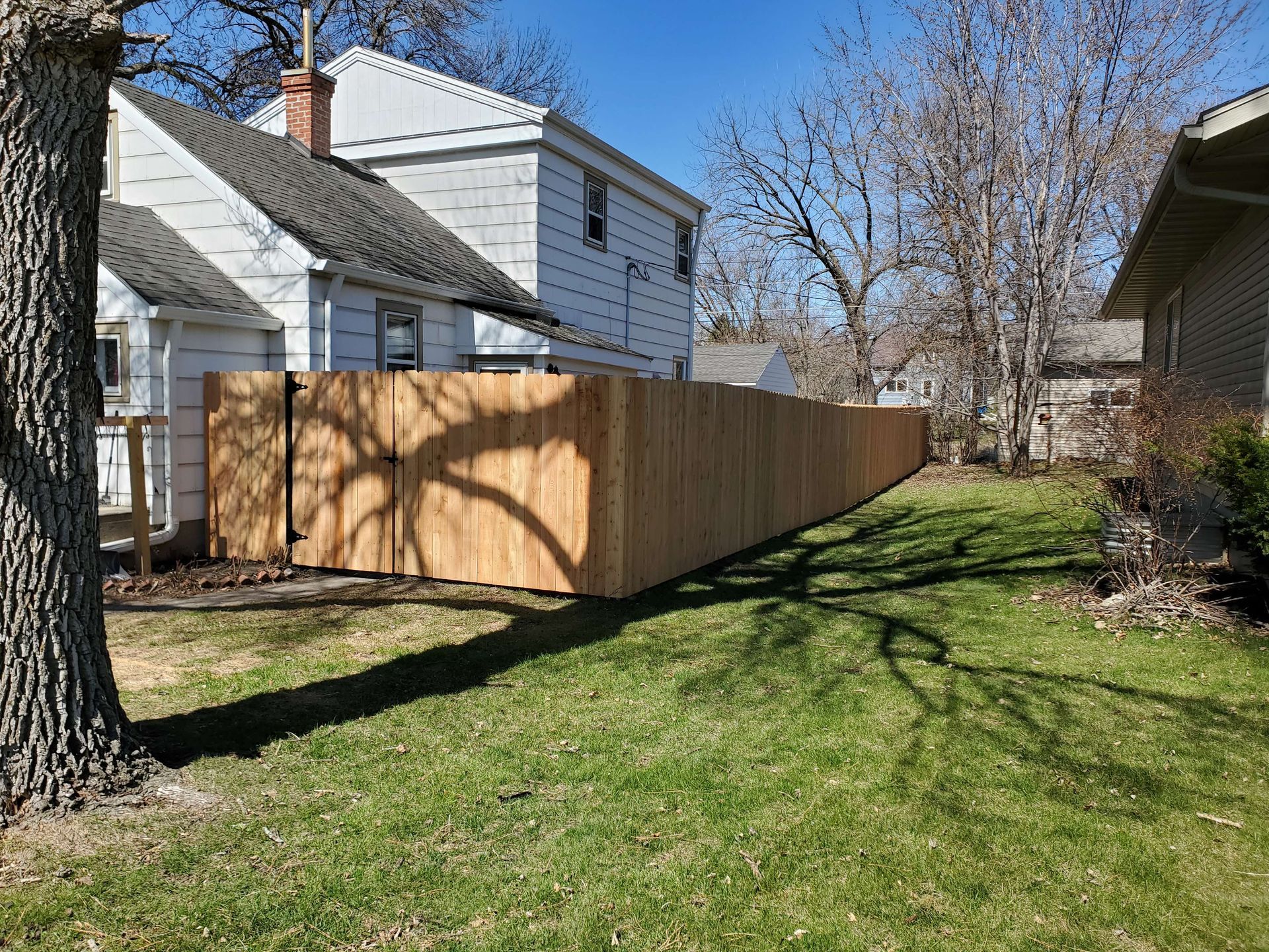 Wooden privacy fence along a grassy side yard beside white houses on a sunny day