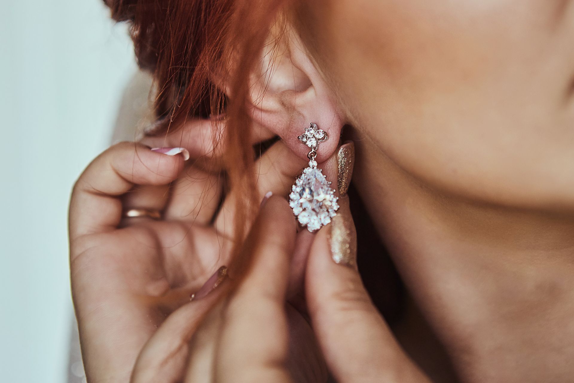 Bride putting on a sparkling teardrop diamond drop earring as part of her bridal jewelry.