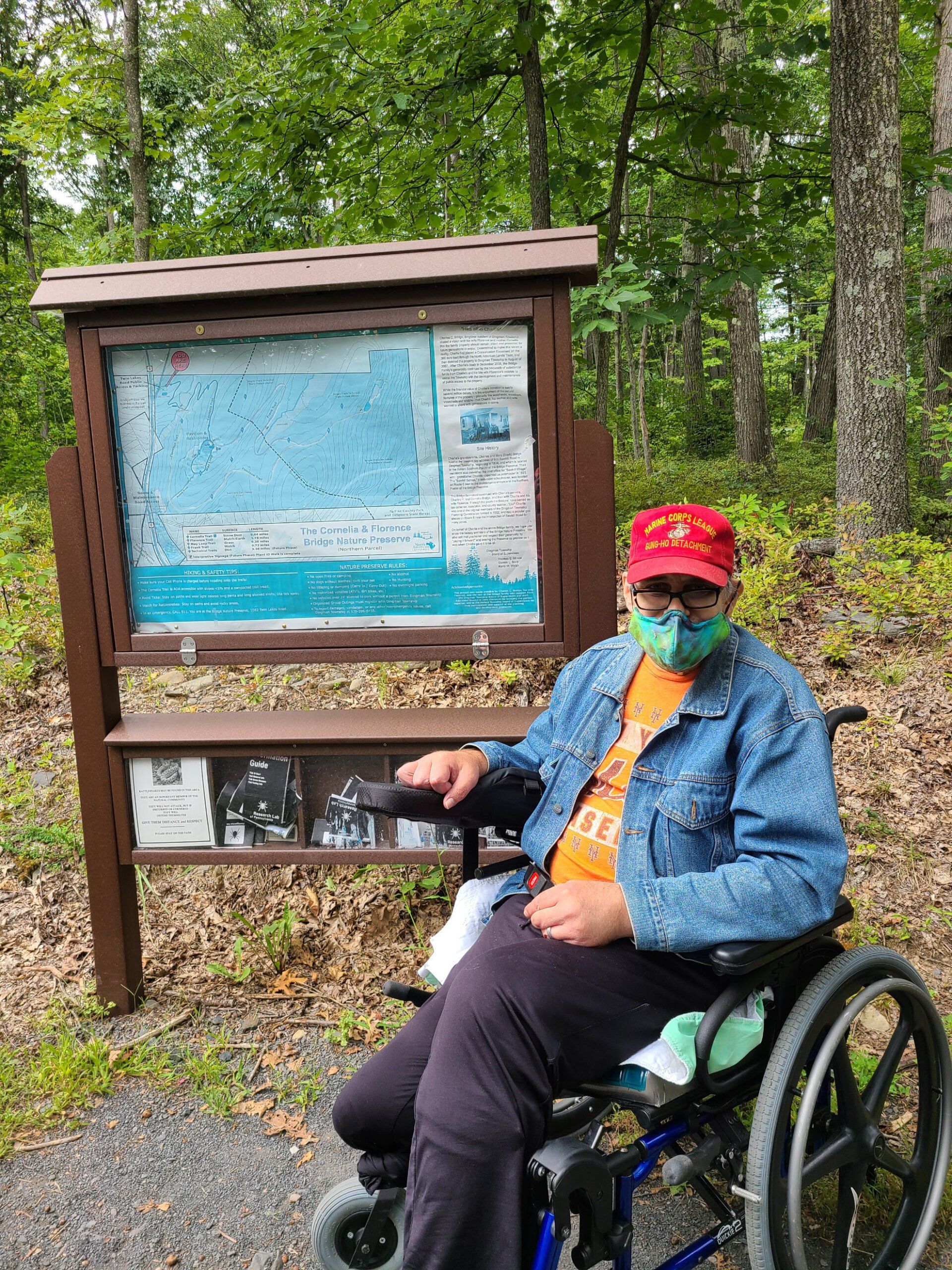 A man in a wheelchair wearing a mask is sitting in front of a map.