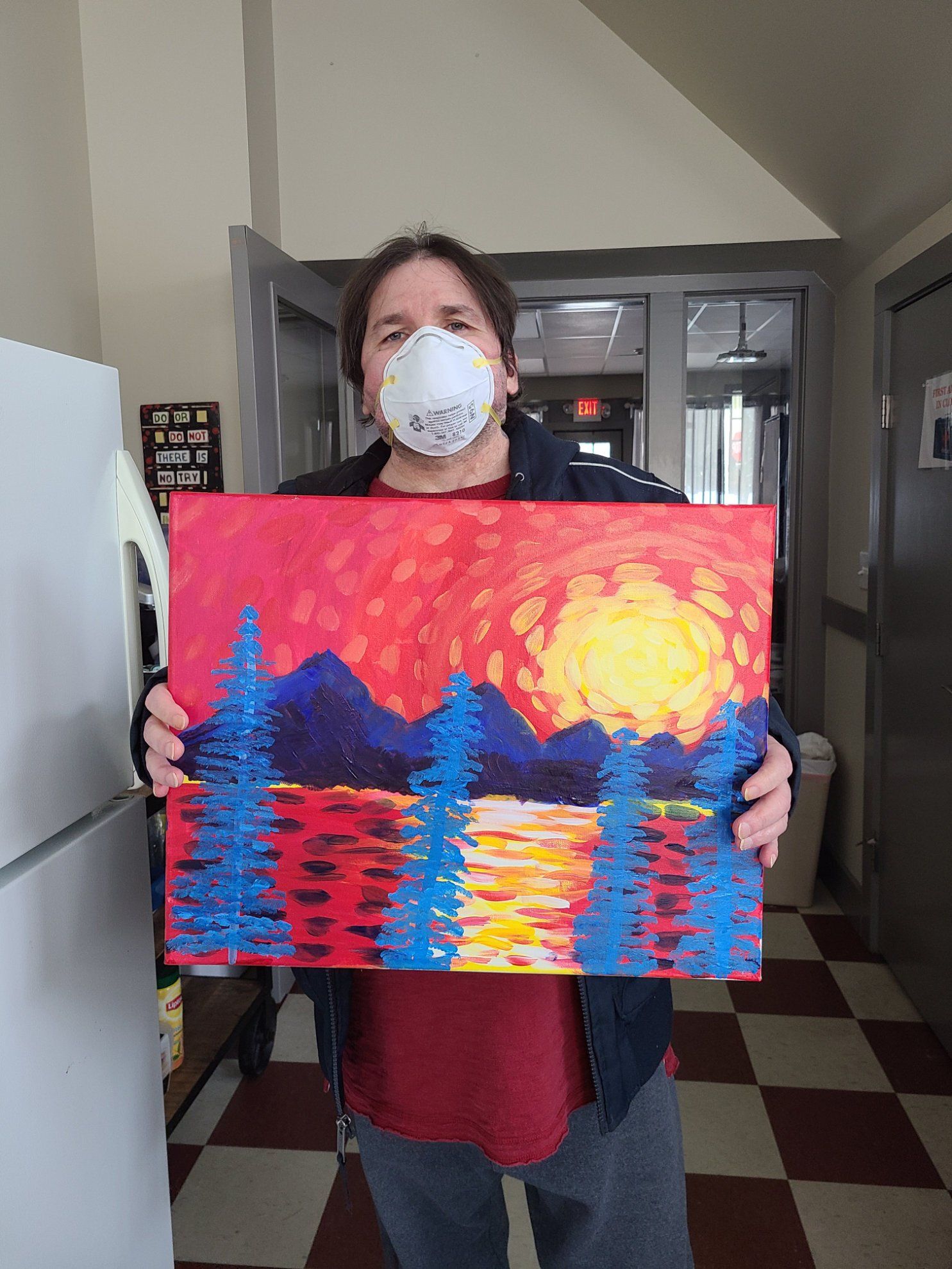 A man wearing a mask is holding a painting of a sunset over a lake.