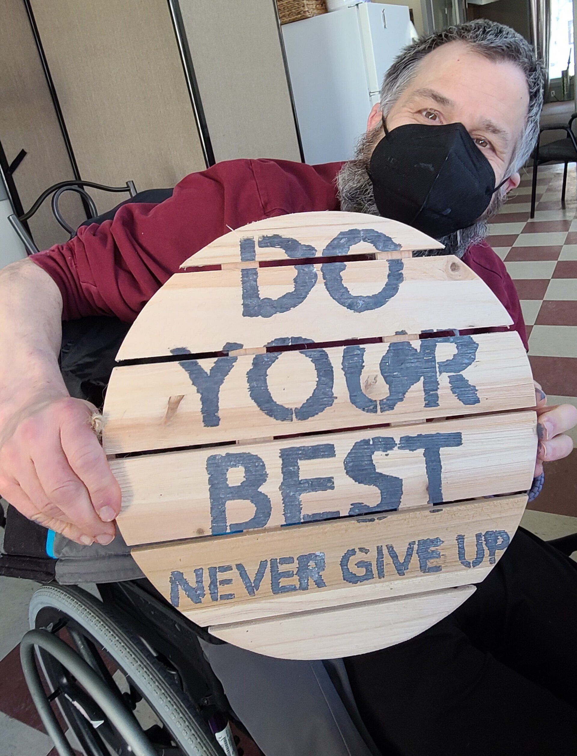 A man in a wheelchair is holding a sign that says do your best never give up