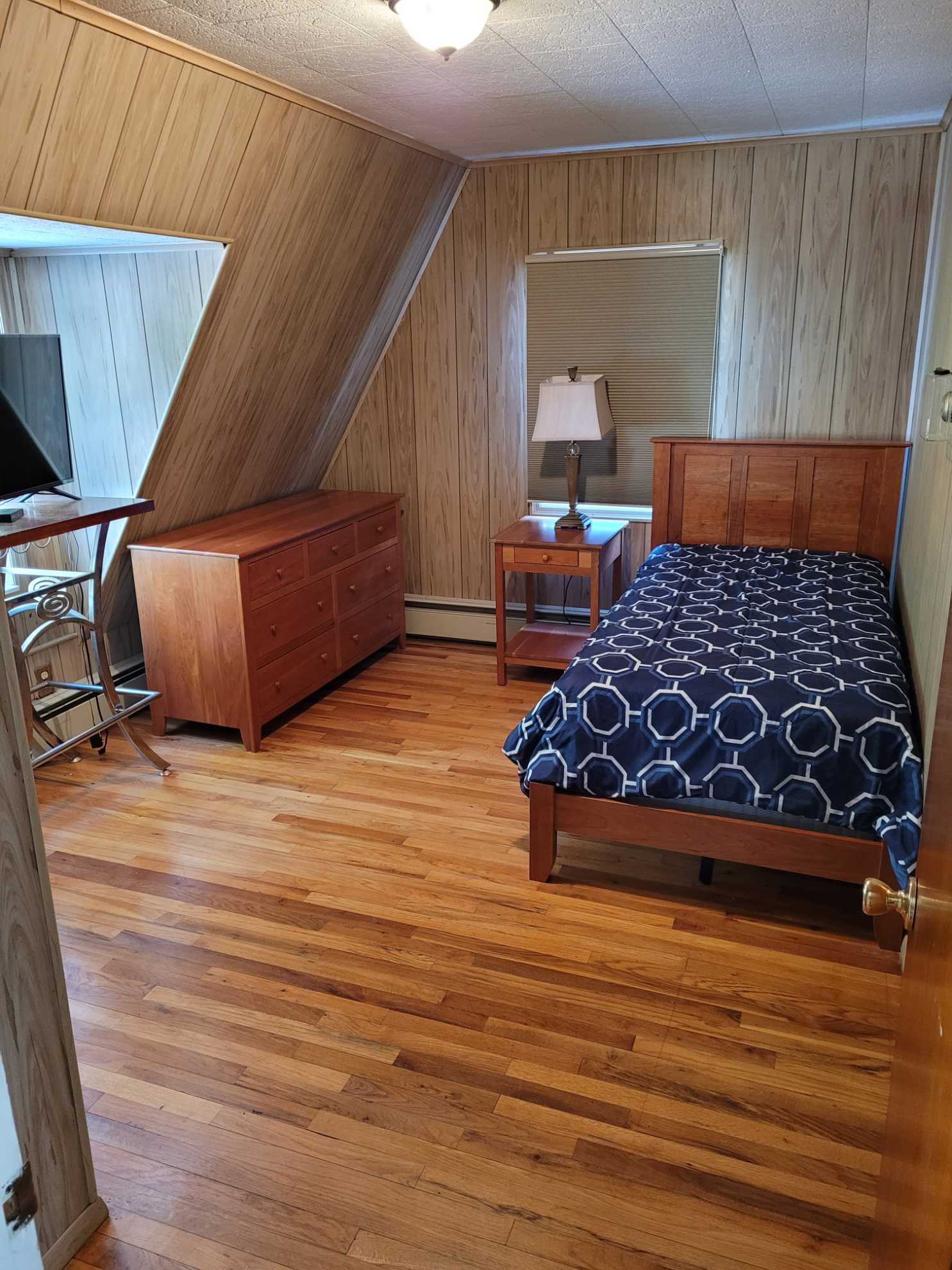 A bedroom with a bed , dresser , nightstand and mirror.