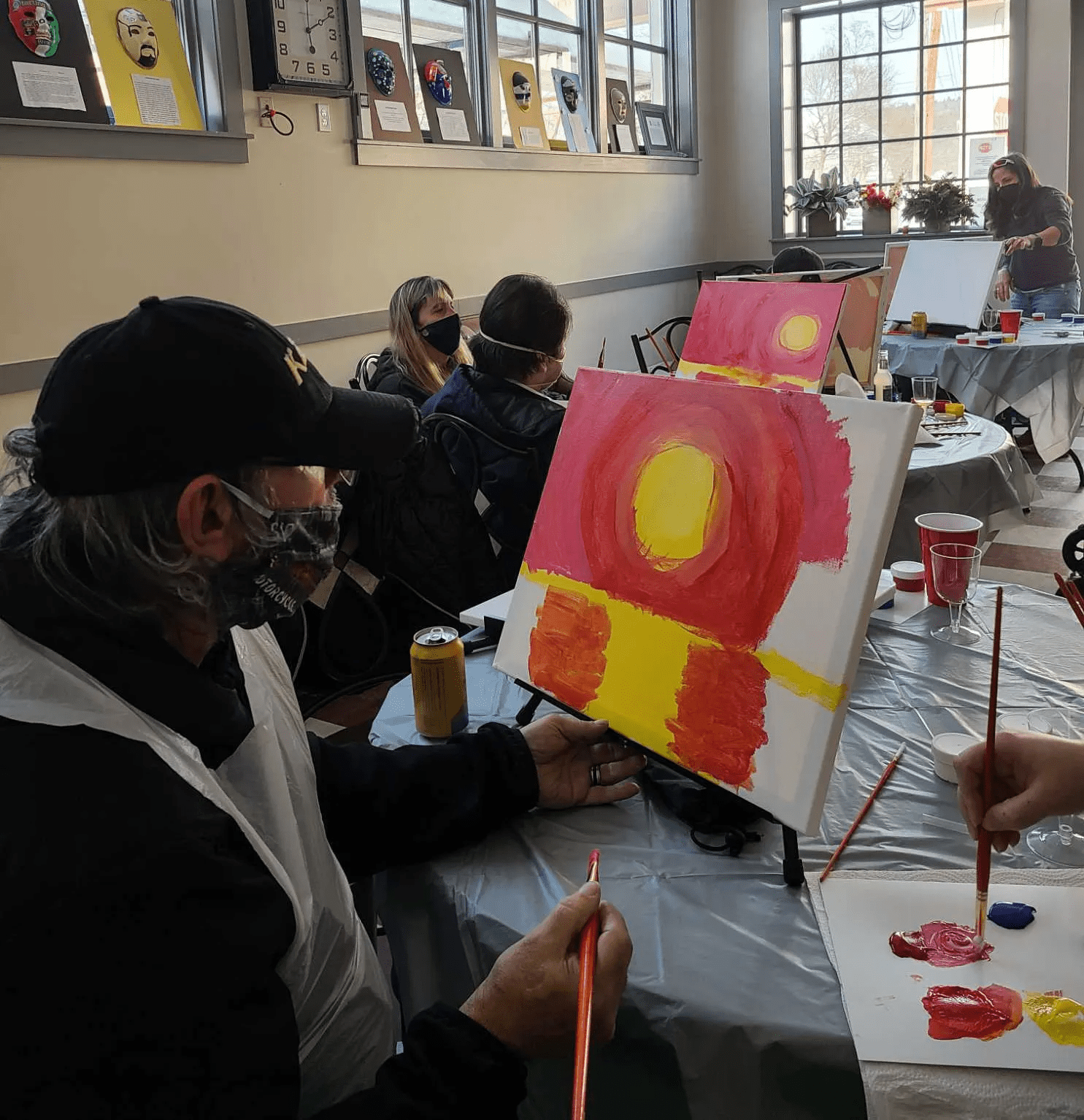 A group of people are sitting at a table painting on canvases