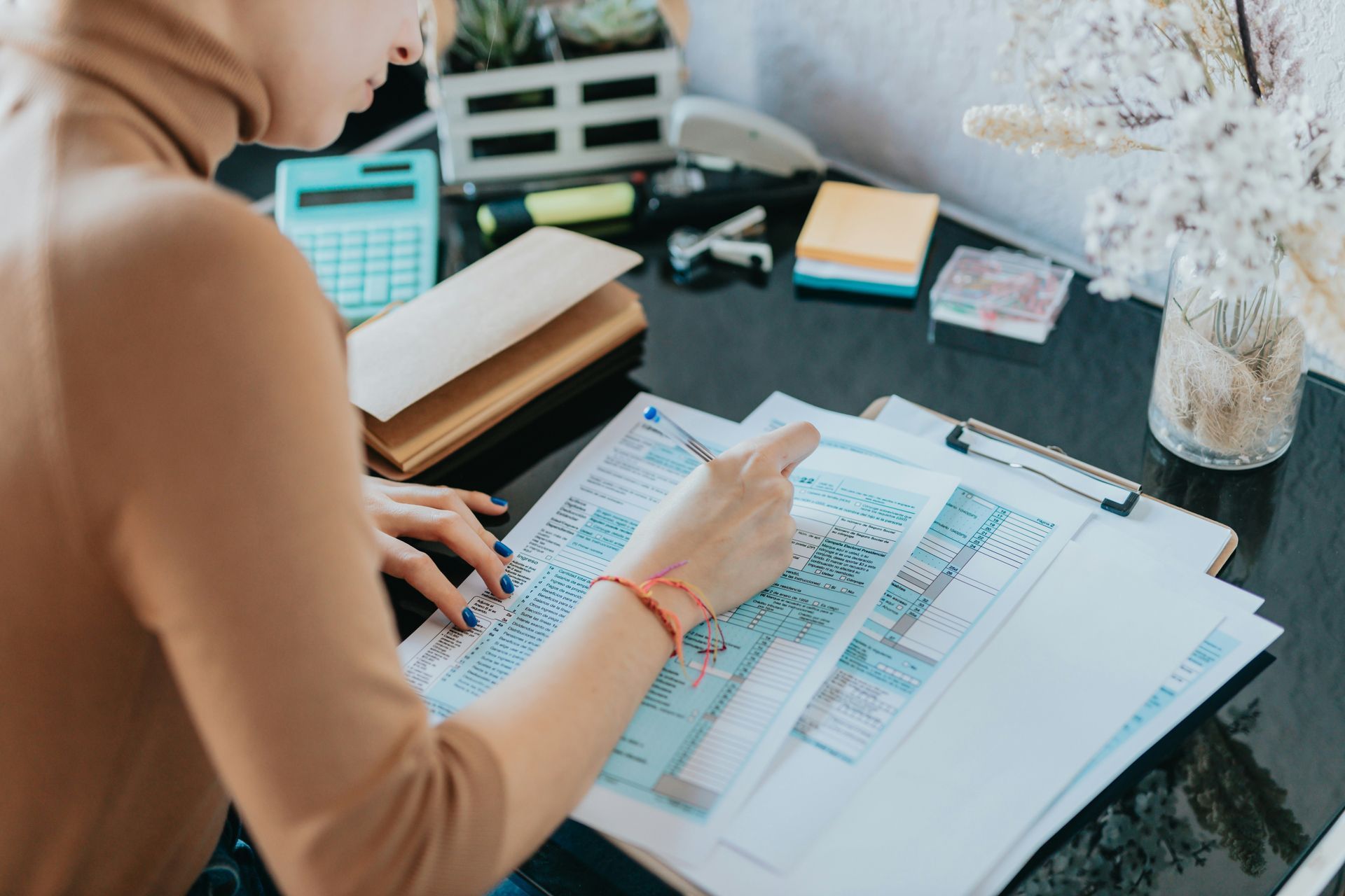 Woman pointing at paperwork on a clipboard, desk with calculator, envelopes, and a vase.