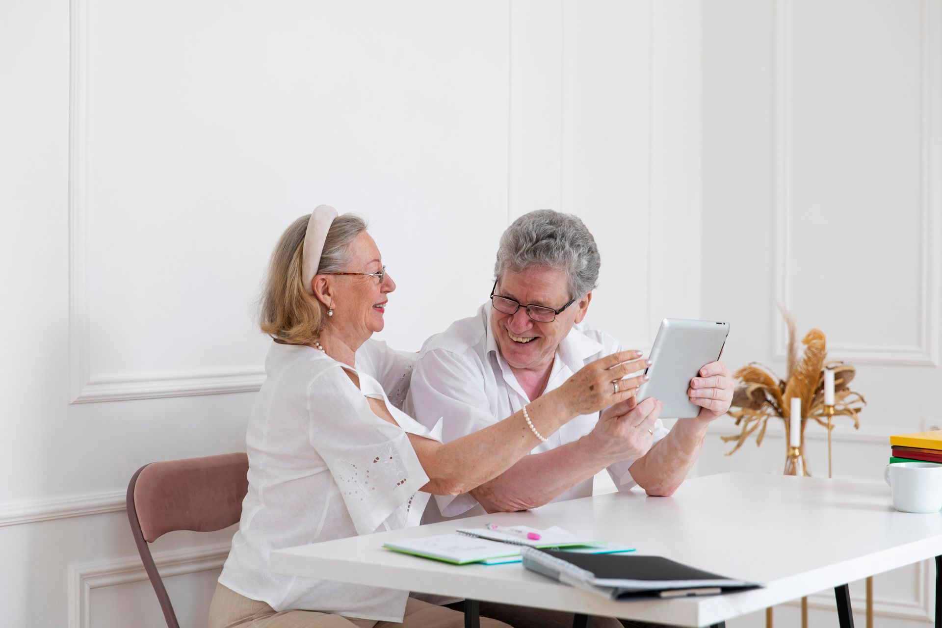 Couple looking at tablet, smiling, at a white table in a bright room.