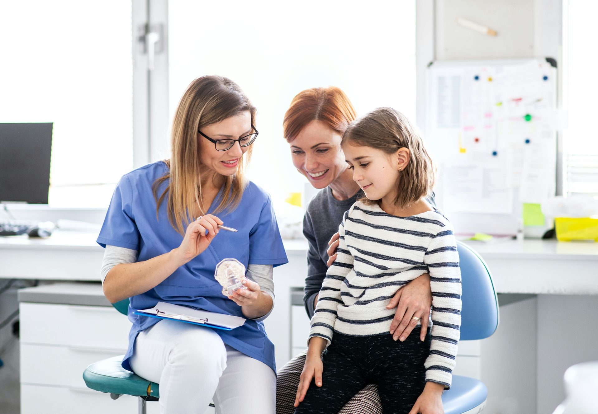 Dentist showing teeth model to a child and parent in dental office.