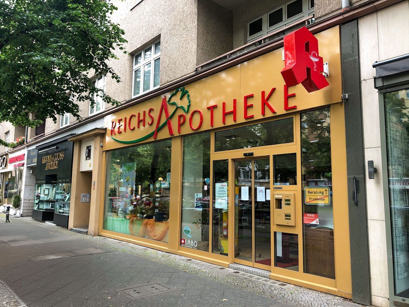 Außenansicht der Reichs Apotheke mit rotem „A“-Logo und Schaufensterdekoration.