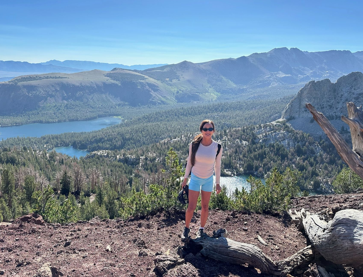 Hiker standing on a rocky overlook above a lake and forested mountains under a clear blue sky