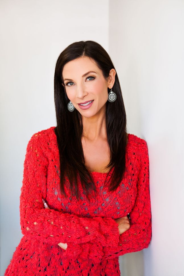 Woman in a bright red dress posing against a white background, smiling gently.