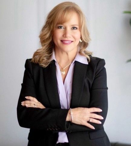 A woman in a black jacket and purple shirt is standing with her arms crossed.
