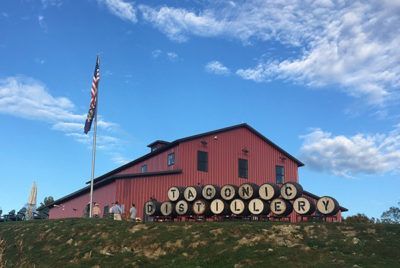 Red Taconic Distillery building with barrels and American flag under blue sky.