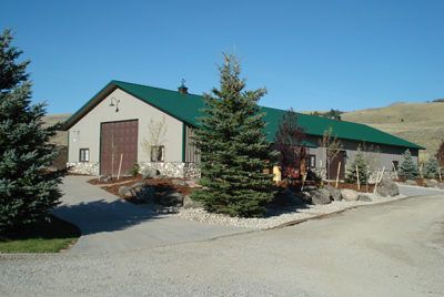 Large beige building with green roof, stone accents, and tall evergreen tree.