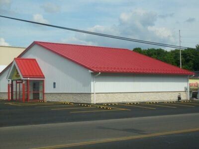A red-roofed building with a white exterior and a small entry area. Set in a parking lot under a cloudy sky.