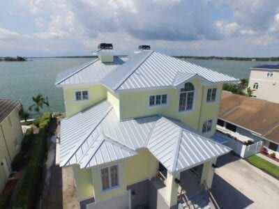 Yellow house with a metal roof overlooking a body of water under a partly cloudy sky.