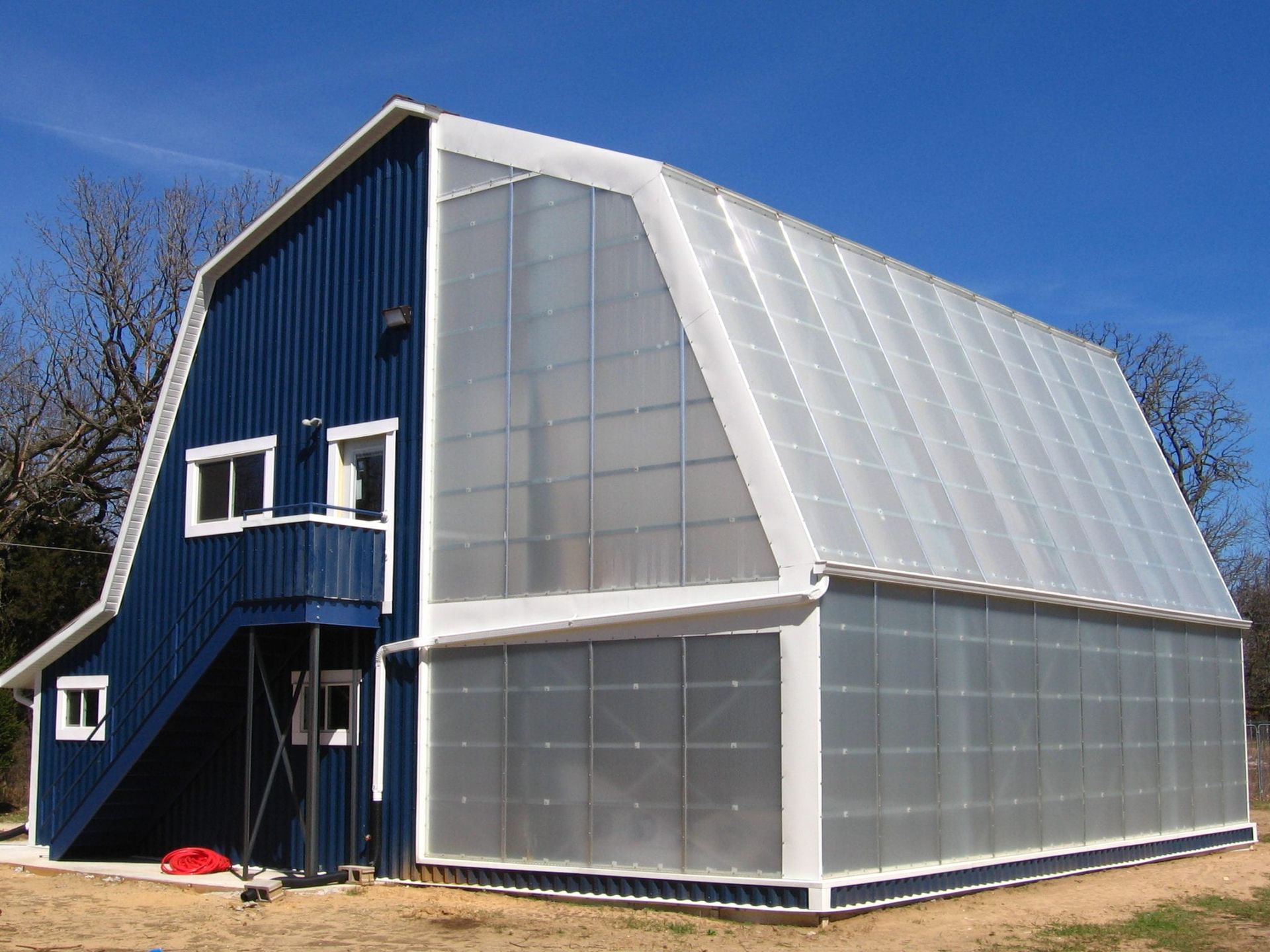 Blue barn-style building with a large, translucent greenhouse attached. White trim and a bright blue sky.