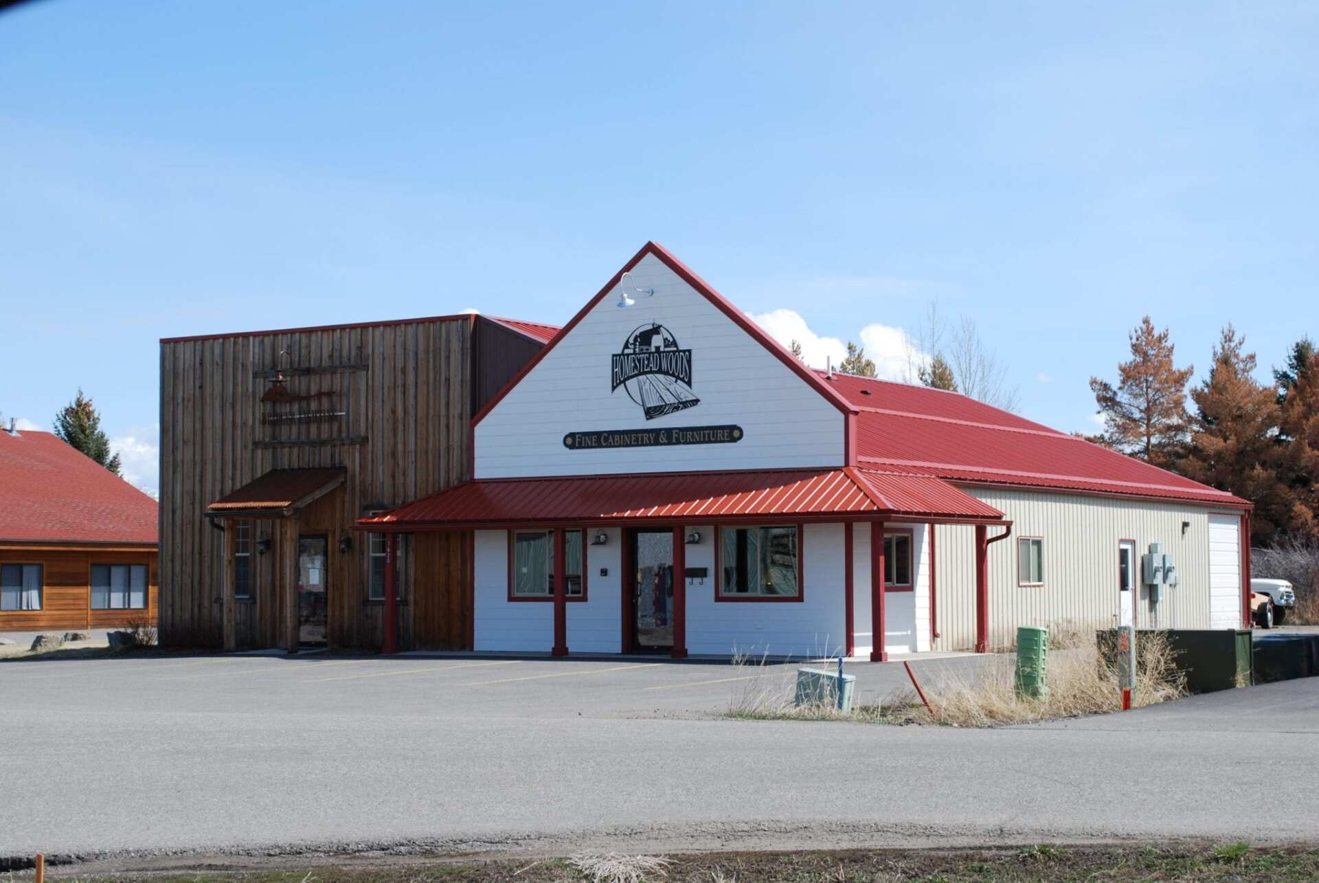 Building with a red roof and white facade, a sign over the door, parked cars in front.