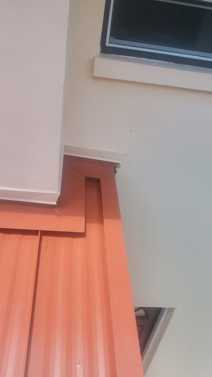 Orange corrugated metal roof meets a beige wall; a white trim piece is above.