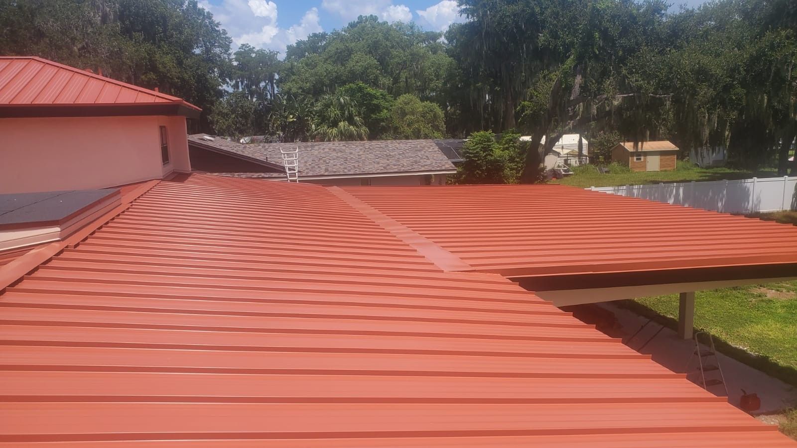 Red metal roof on a building, with trees and sky in the background.