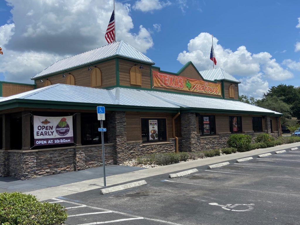 Texas Roadhouse restaurant, exterior view. Brick and wood facade, flags, parking lot.