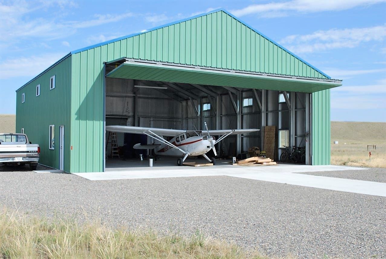 Green metal airplane hangar with a small plane inside and an open door.