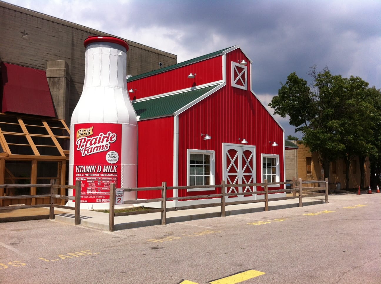 Red barn-shaped building with a giant milk bottle, likely a dairy store, in front of a parking lot.
