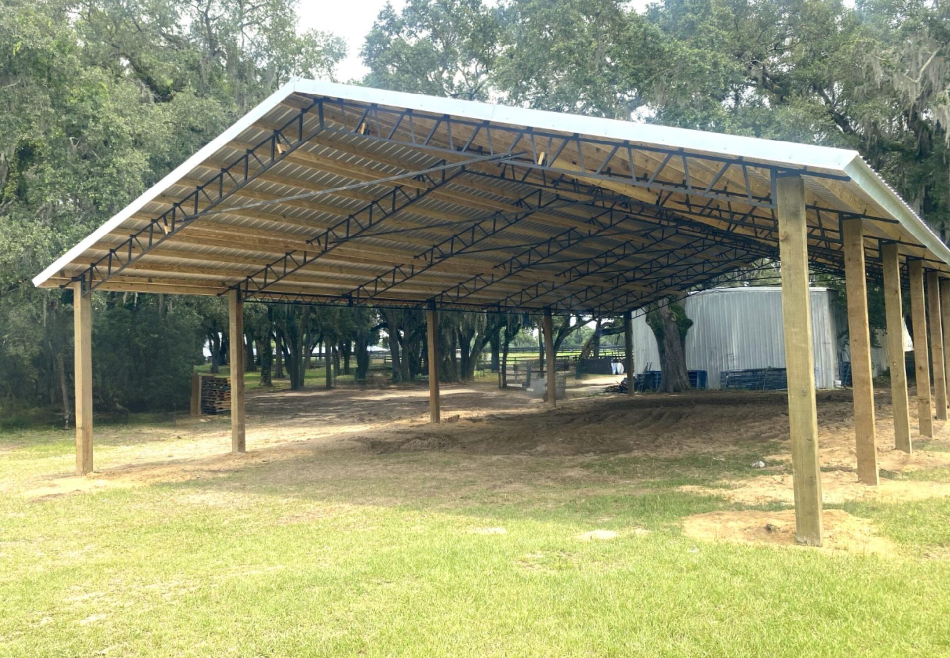Large open-air shed with metal roof and wooden supports in a grassy outdoor area.