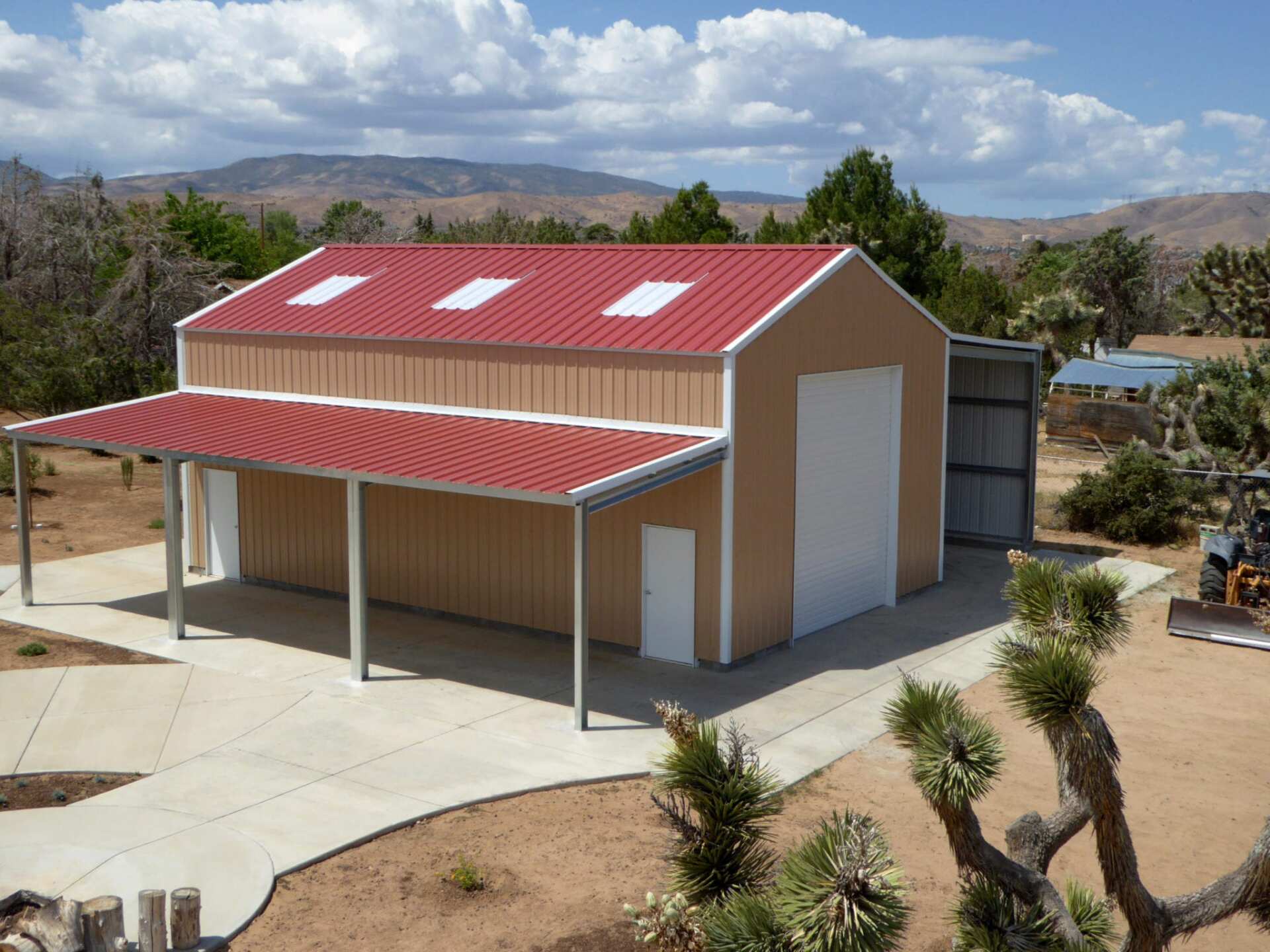 Tan metal building with a red roof and a carport, set against a mountain backdrop.