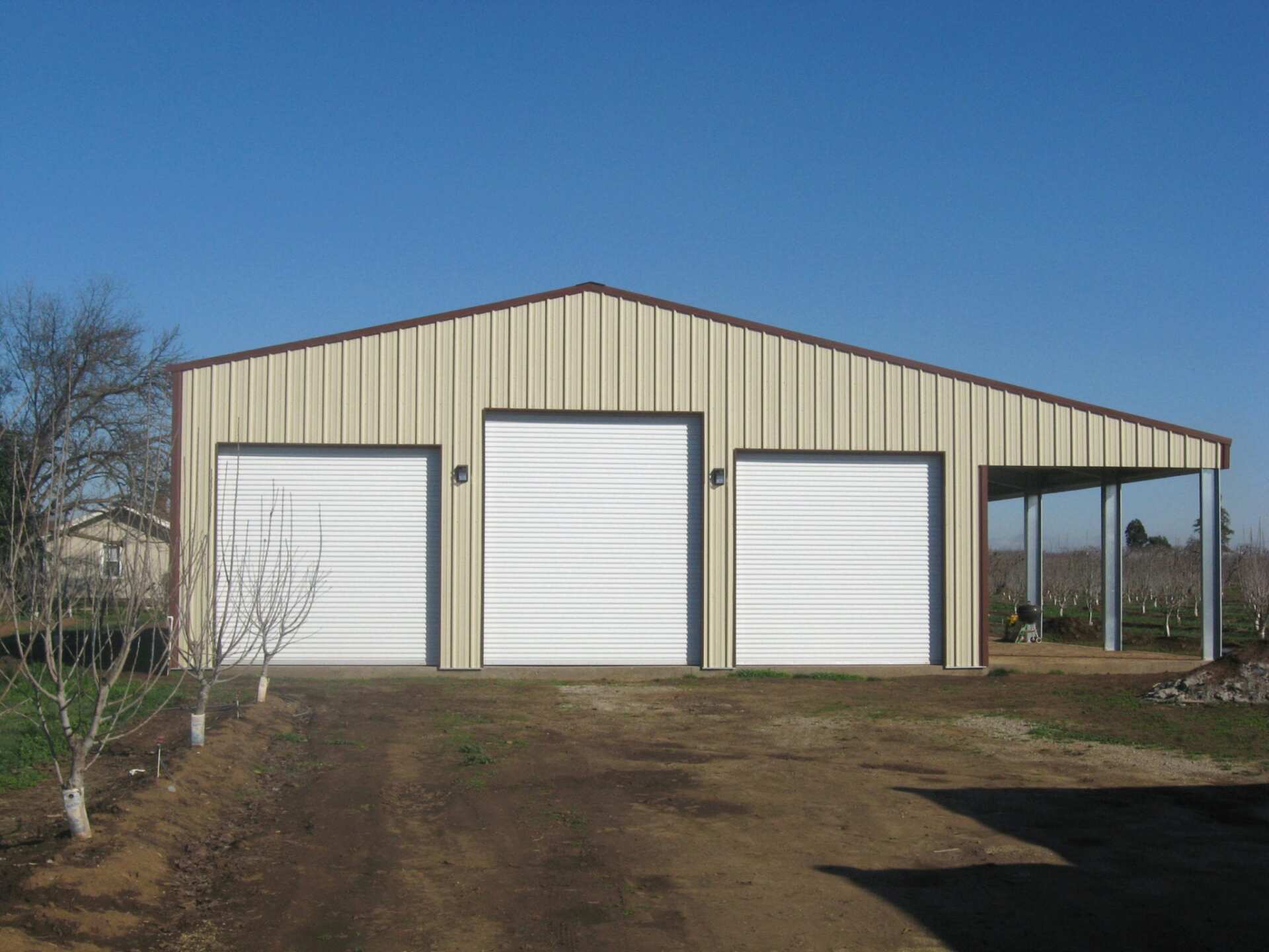 Three-bay metal garage with tan walls, brown trim, and white garage doors; a lean-to on the right.