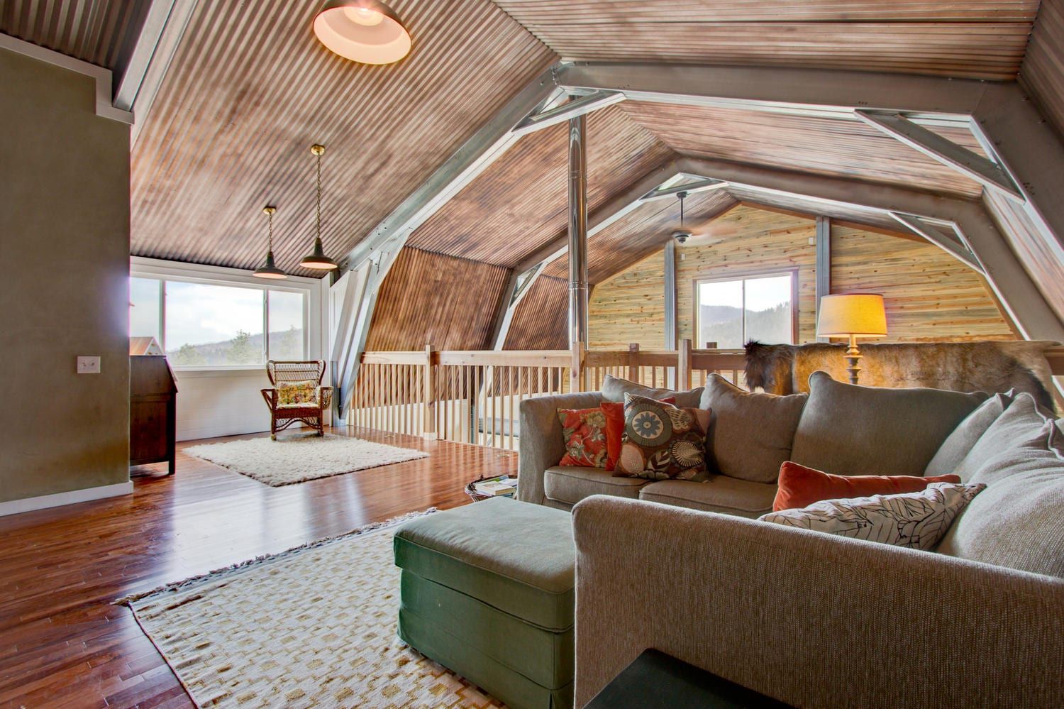 Living room in a loft with wood paneling, a sofa, a rug, and windows.