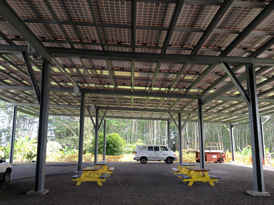 Covered parking area with solar panels, picnic tables, and a white van parked in the gravel lot.