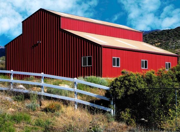 Red metal barn with white trim, white fence, against a mountain backdrop.