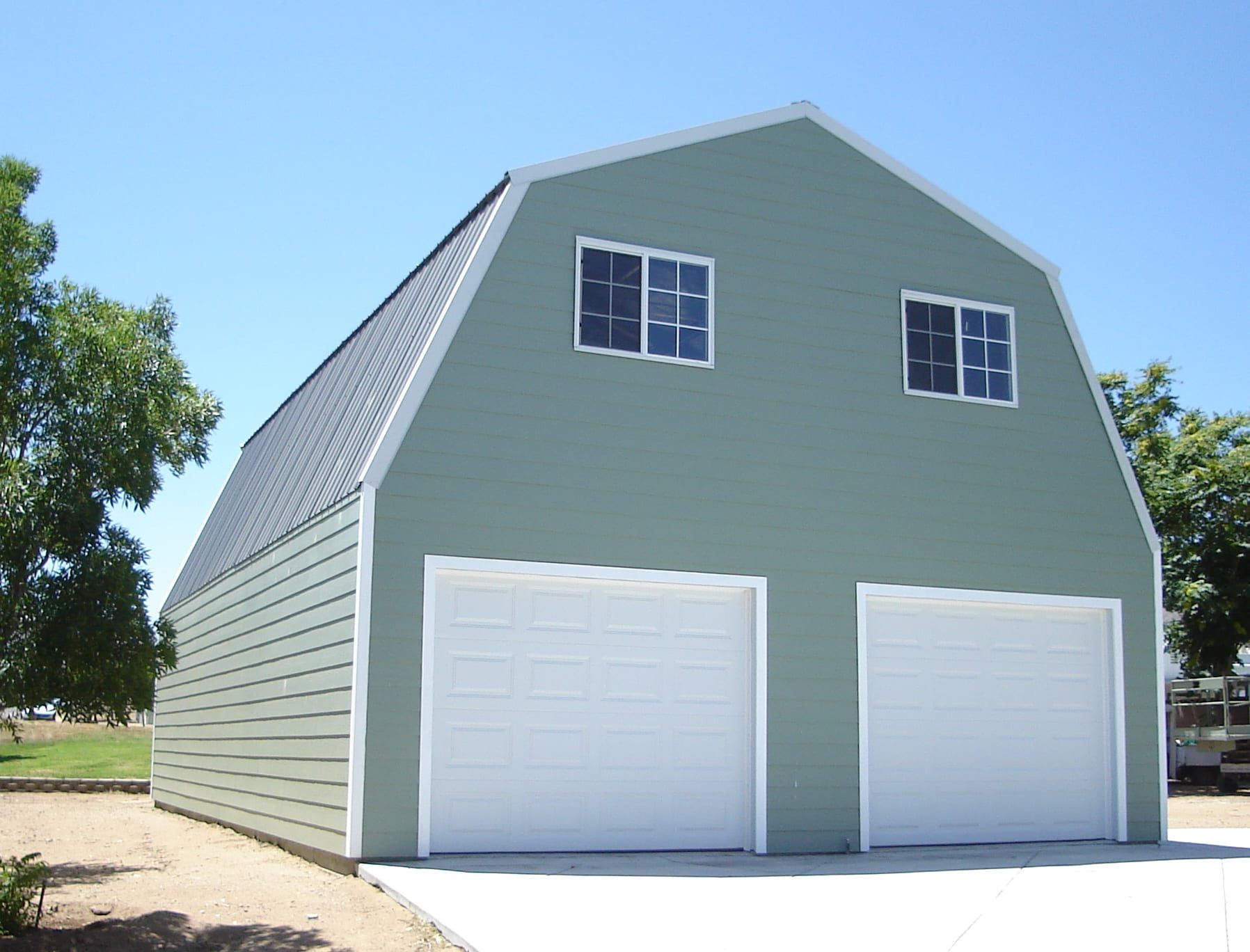 Green two-story barn-style garage with white garage doors, windows, and a black roof.