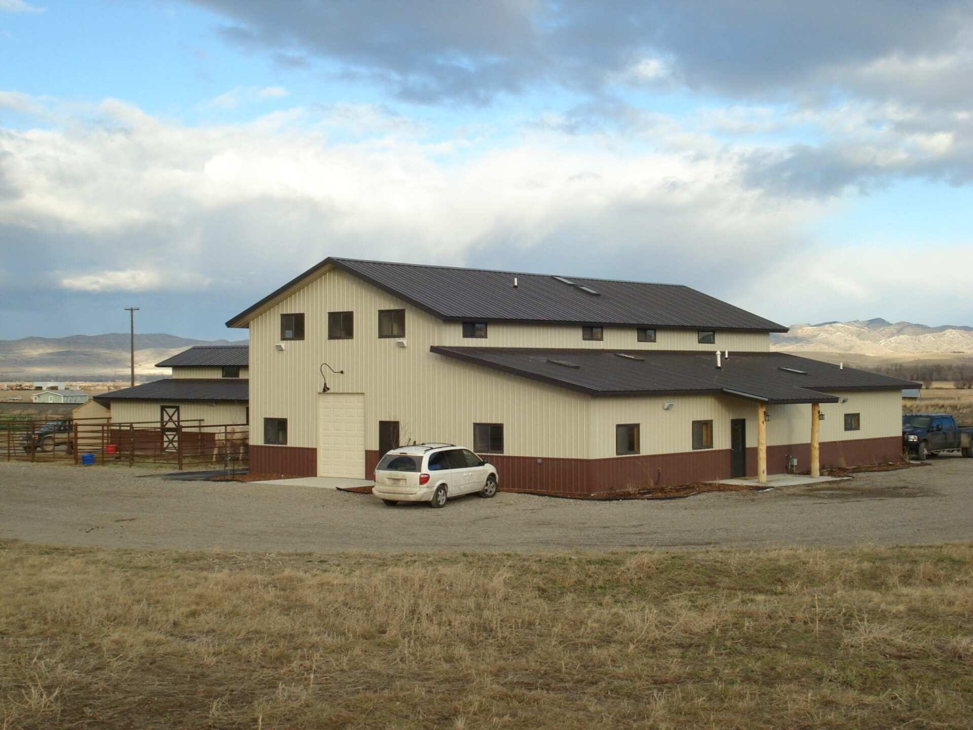 A large, light-colored building with brown trim and dark roof under a cloudy sky, a white van is parked outside.